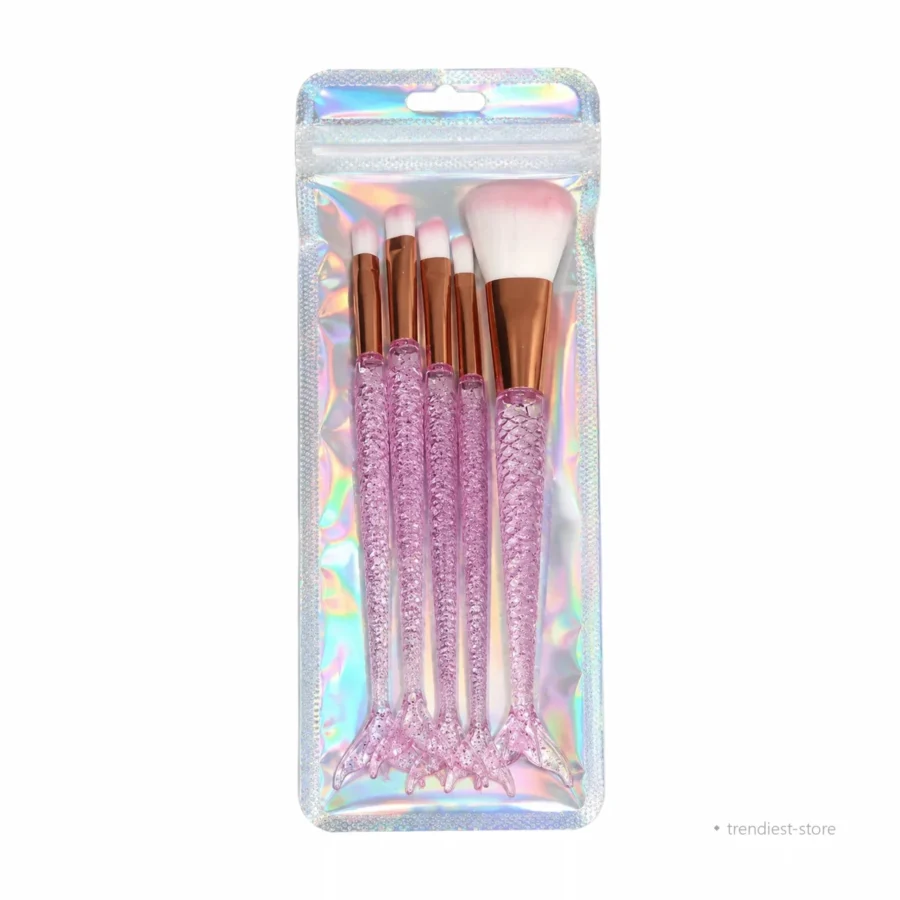 A set of five makeup brushes in a clear holographic zip pouch. The brushes have white bristles with a soft pink gradient, rose gold ferrules, and glittery pink mermaid tail handles.
