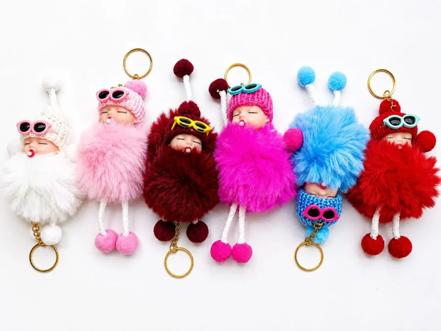 Six sleeping baby doll pom pom keychains in white, pink, maroon, hot pink, blue and red